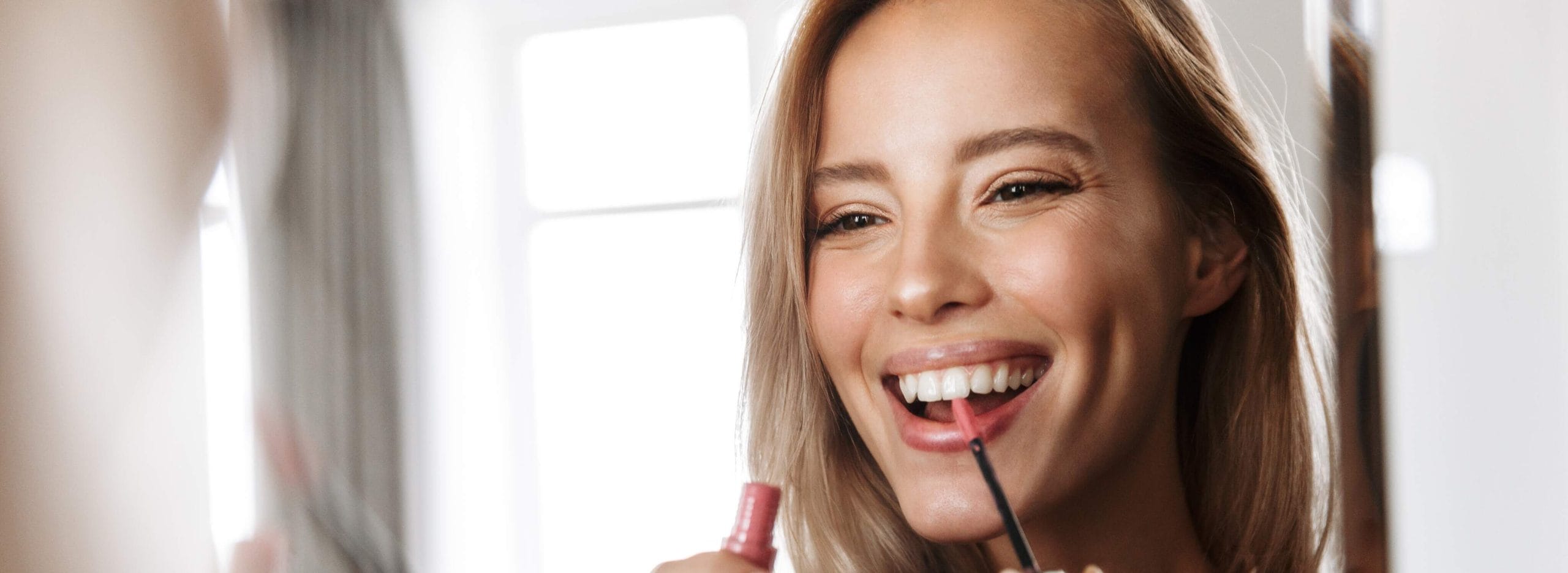 A woman applies makeup while smiling.