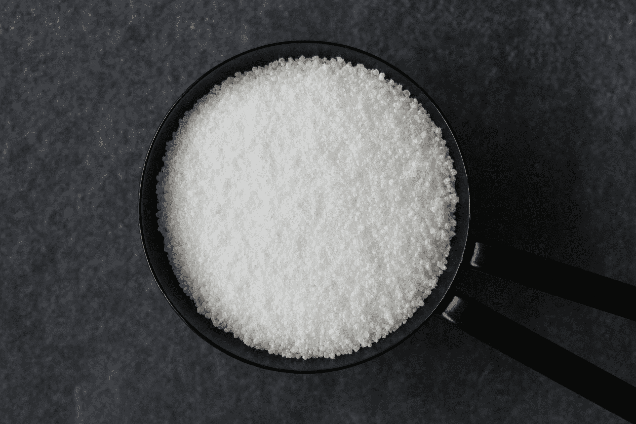 a bowl of white citric acid on a black background (probably a table)
