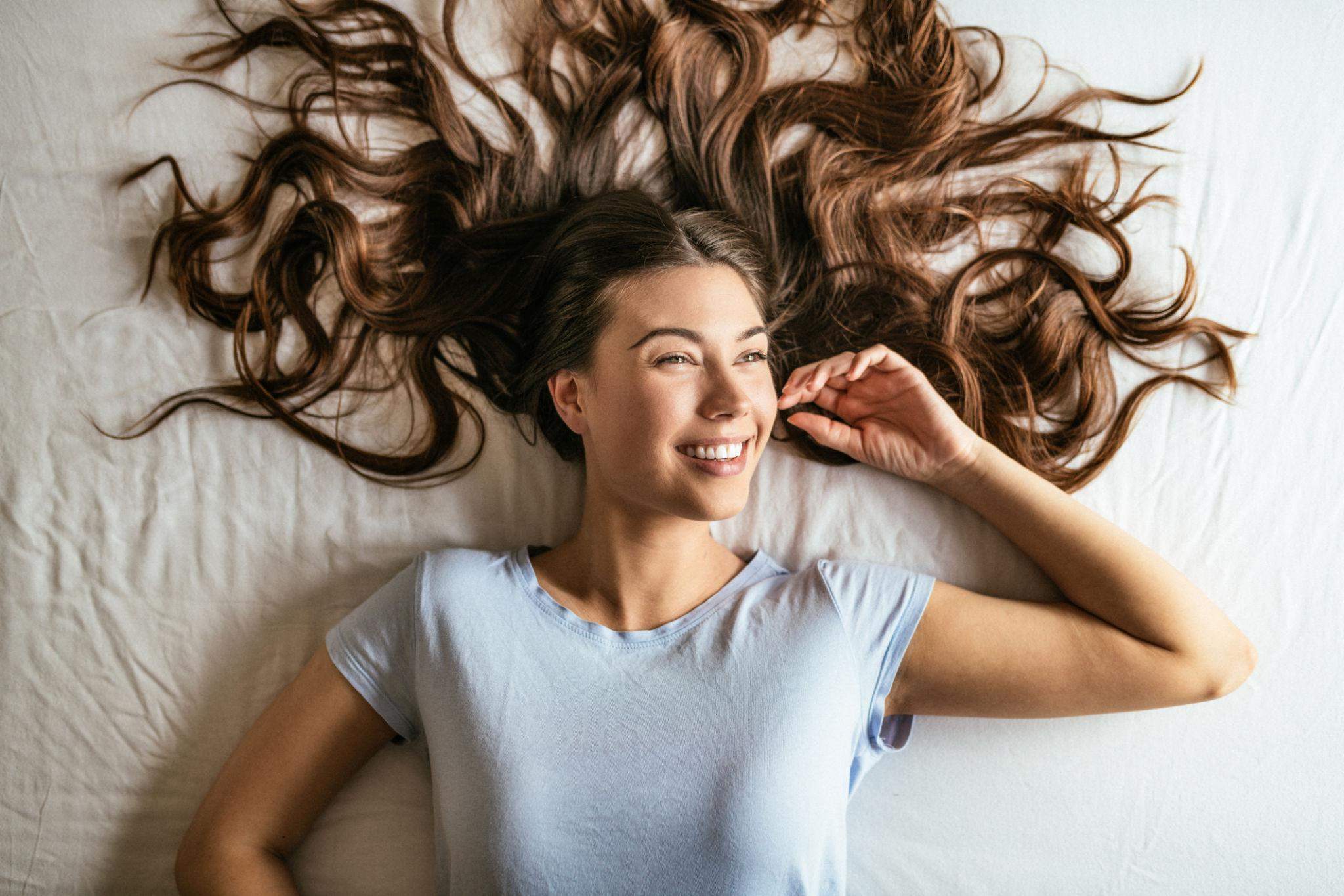 beautiful curly_haired woman sitting on a bed. View from above