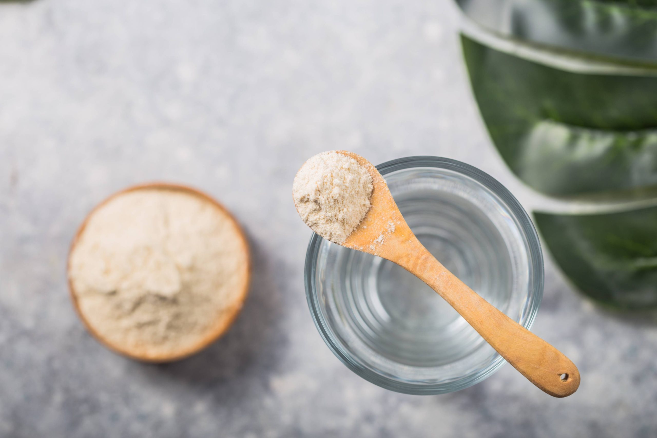 Glass of water, collagen powder on white table.