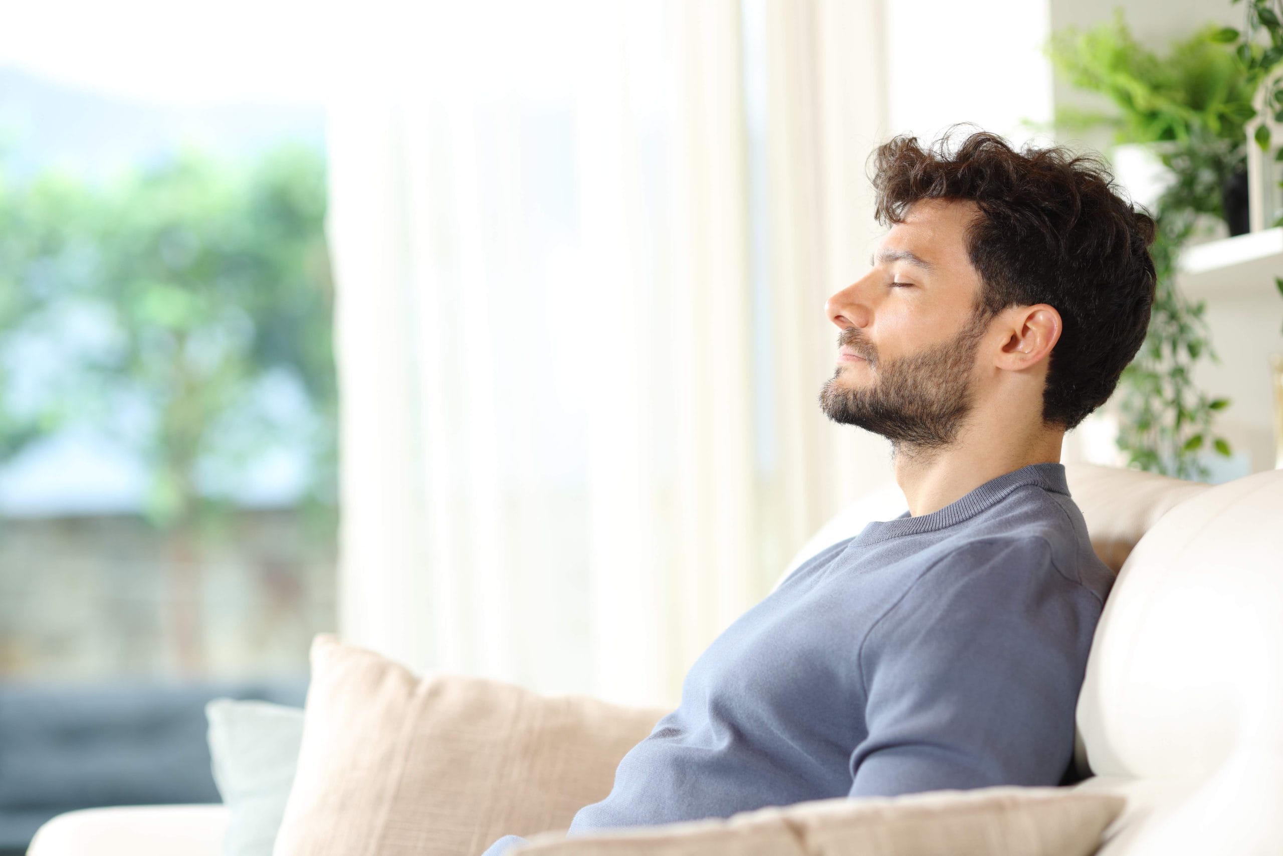 Serious relaxed man breathing fresh air sitting on a couch at home