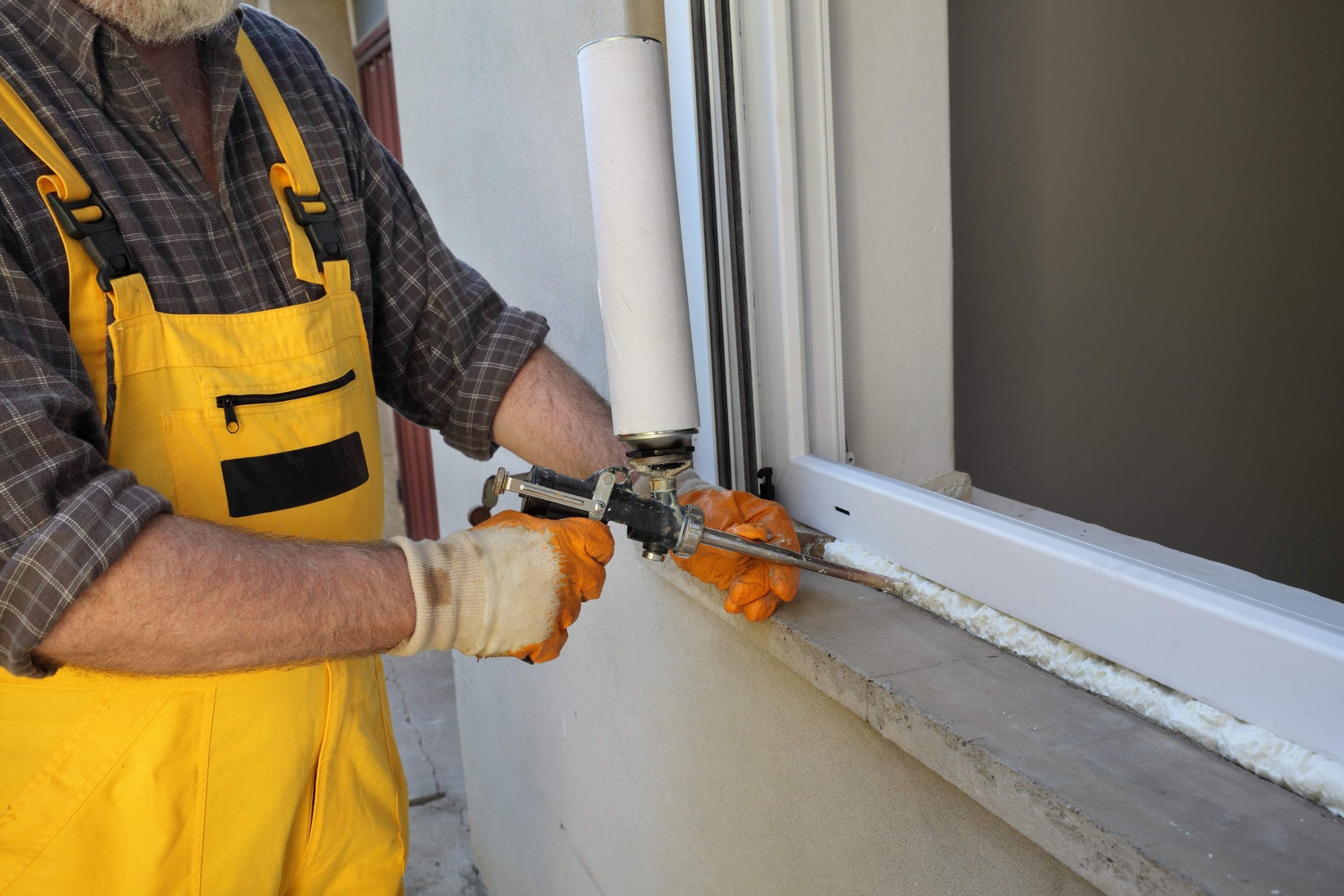Worker installing new plastic window, using handgun with polyurethane foam