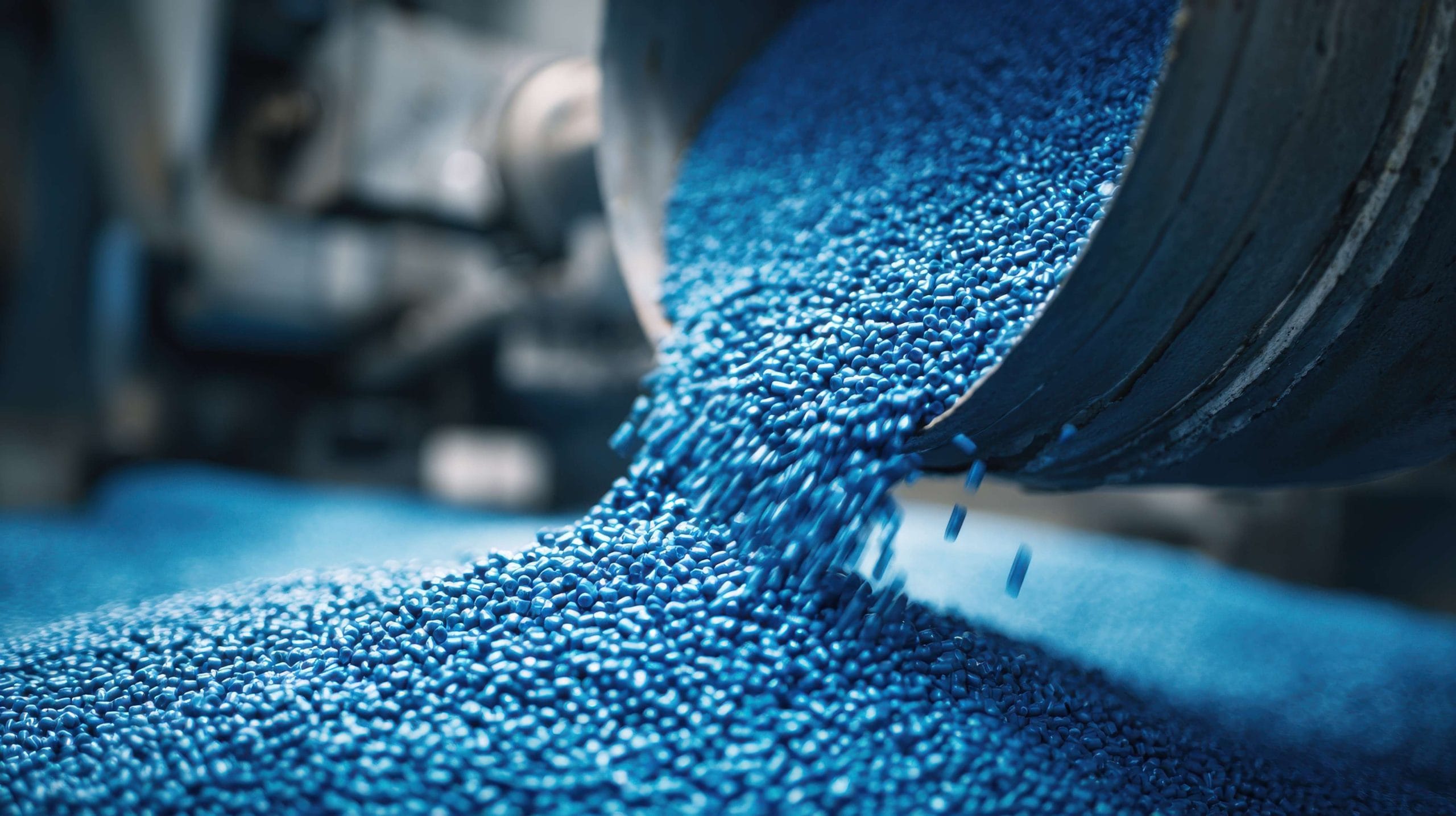 Close-up of blue plastic pellets pouring from an industrial hopper, raw materials for manufacturing process