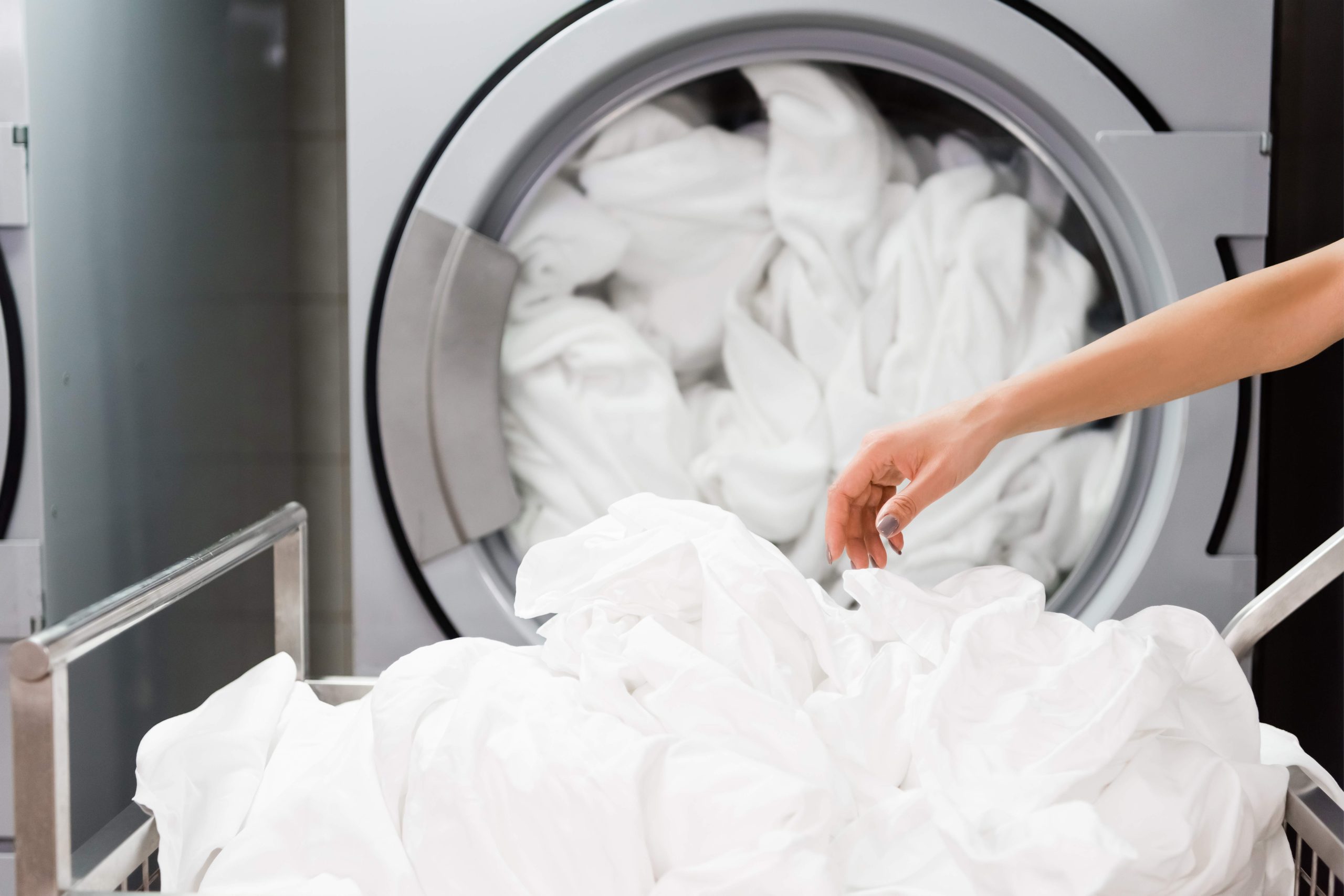cropped view of housemaid near white bed sheets in laundry