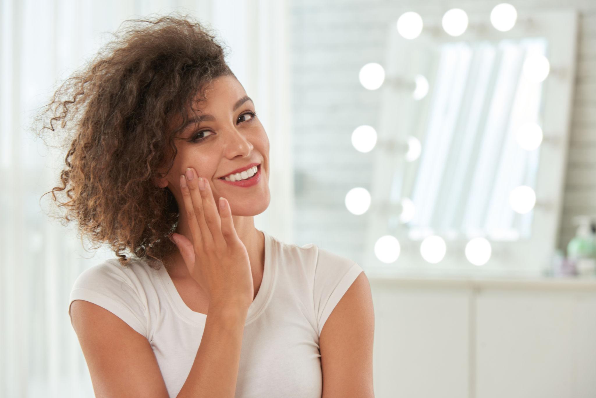 woman applying skincare treatment on her face smiling