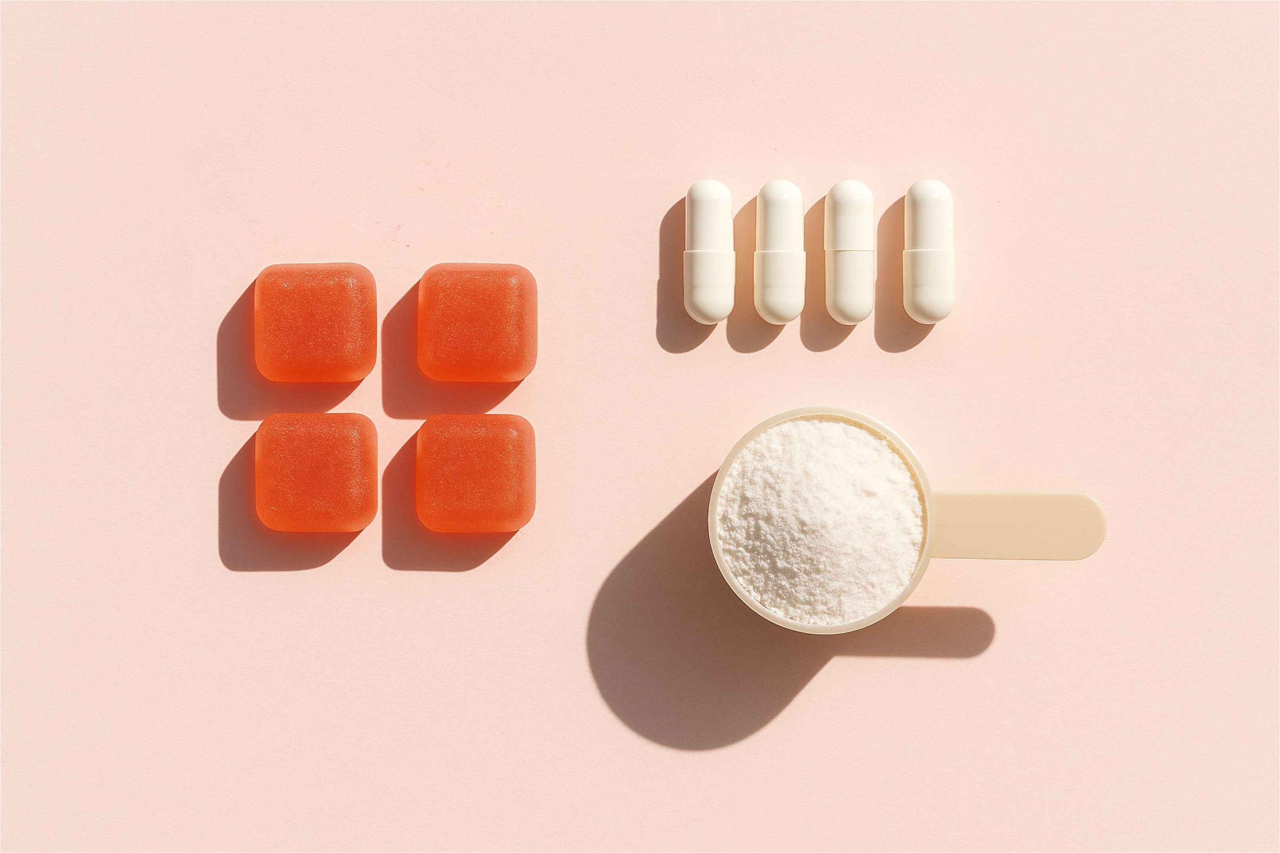 various forms of dietary supplements including square orange gummies white capsules and a scoop of white collagen powder representing different choices for daily wellness and health