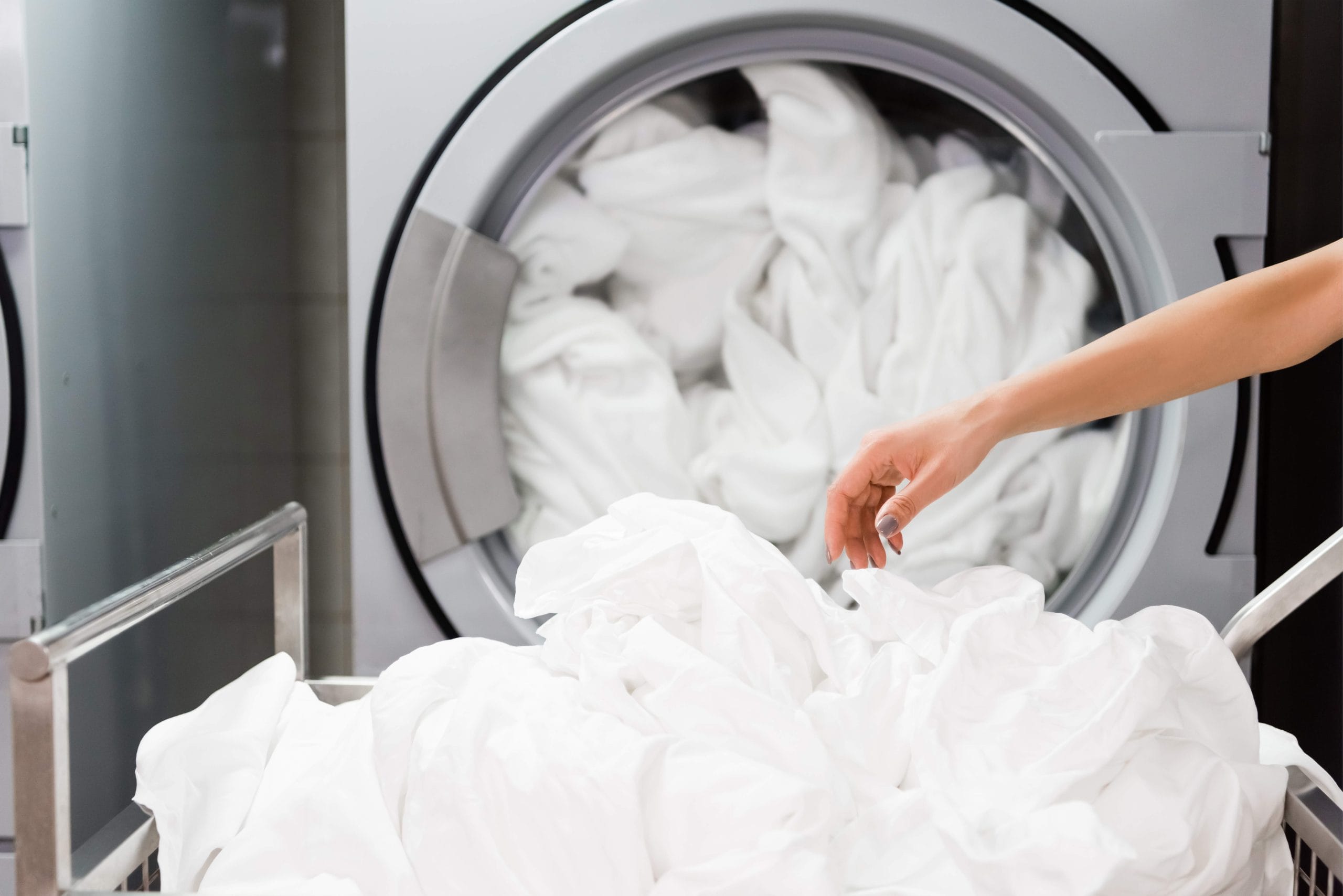 cropped view of housemaid near white bed sheets in laundry