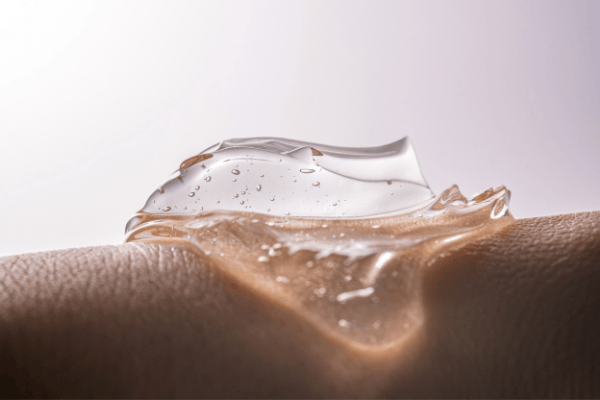 Clear cosmetic gel being drawn from a beaker, showing the short flow and transparency that carbomer alternatives are selected to reproduce.