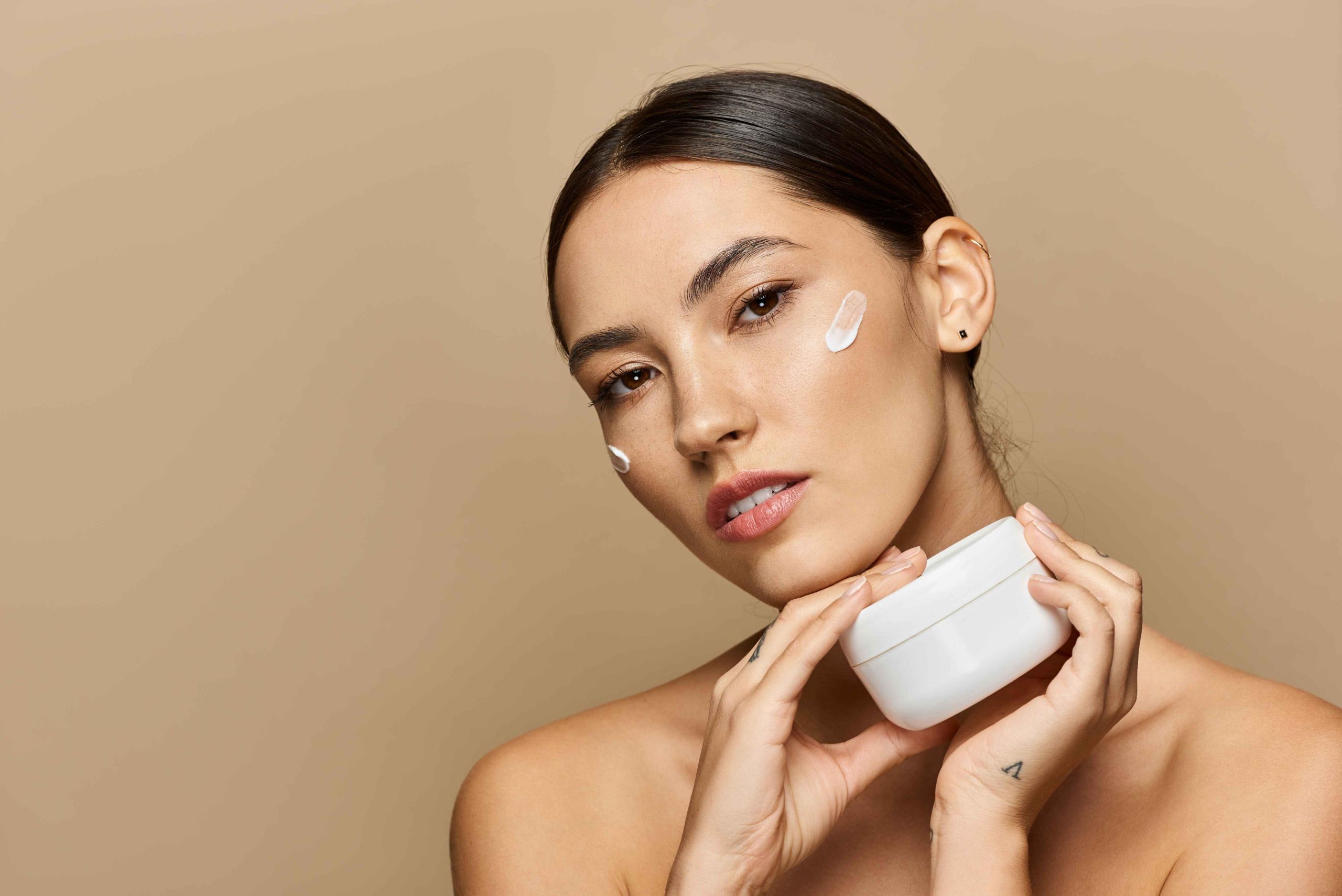 Brunette woman applies cream thoughtfully while highlighting her radiant skin in a serene setting.