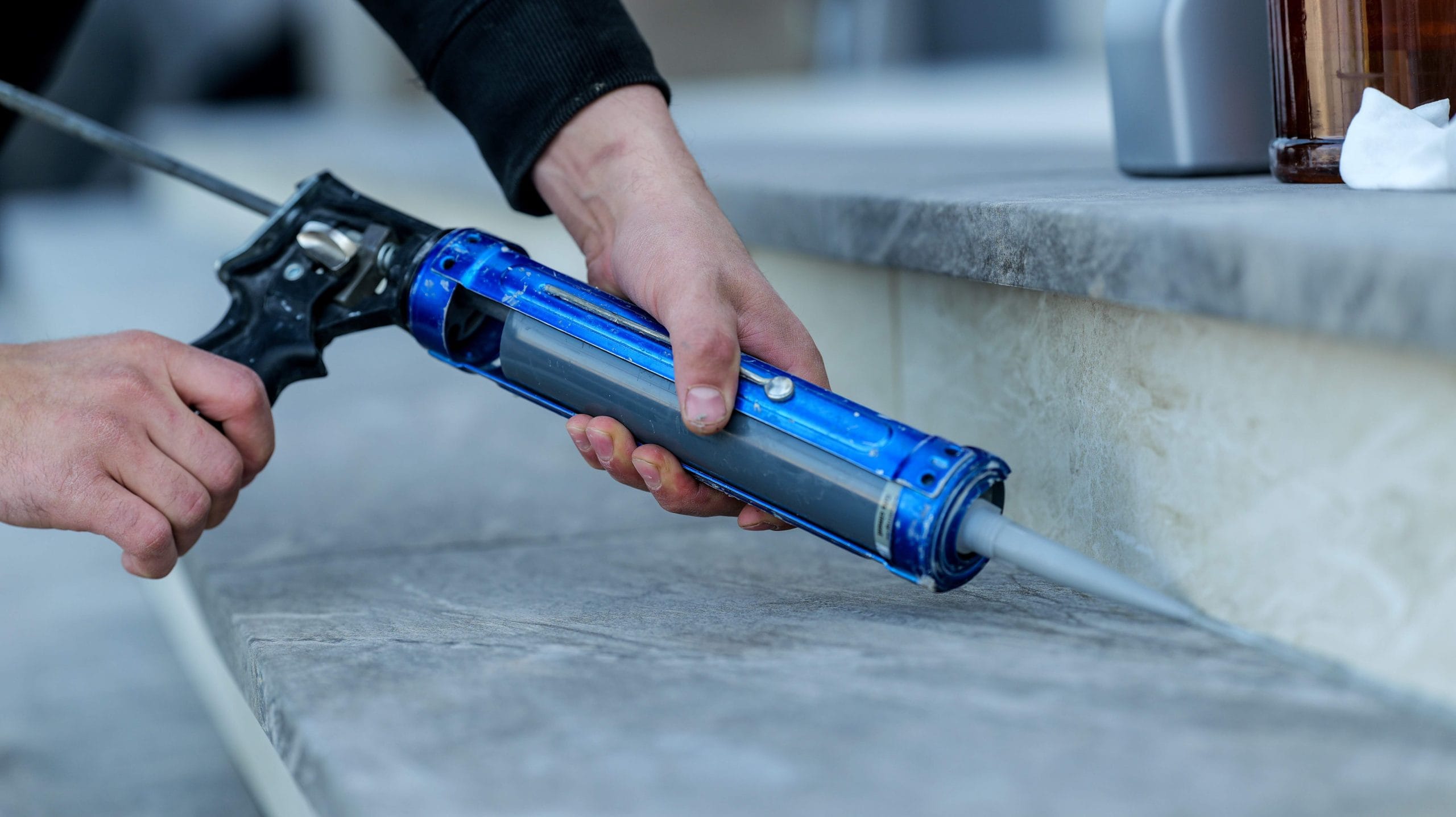 A person is using a caulk gun to apply sealant to a surface, likely for sealing or filling gaps