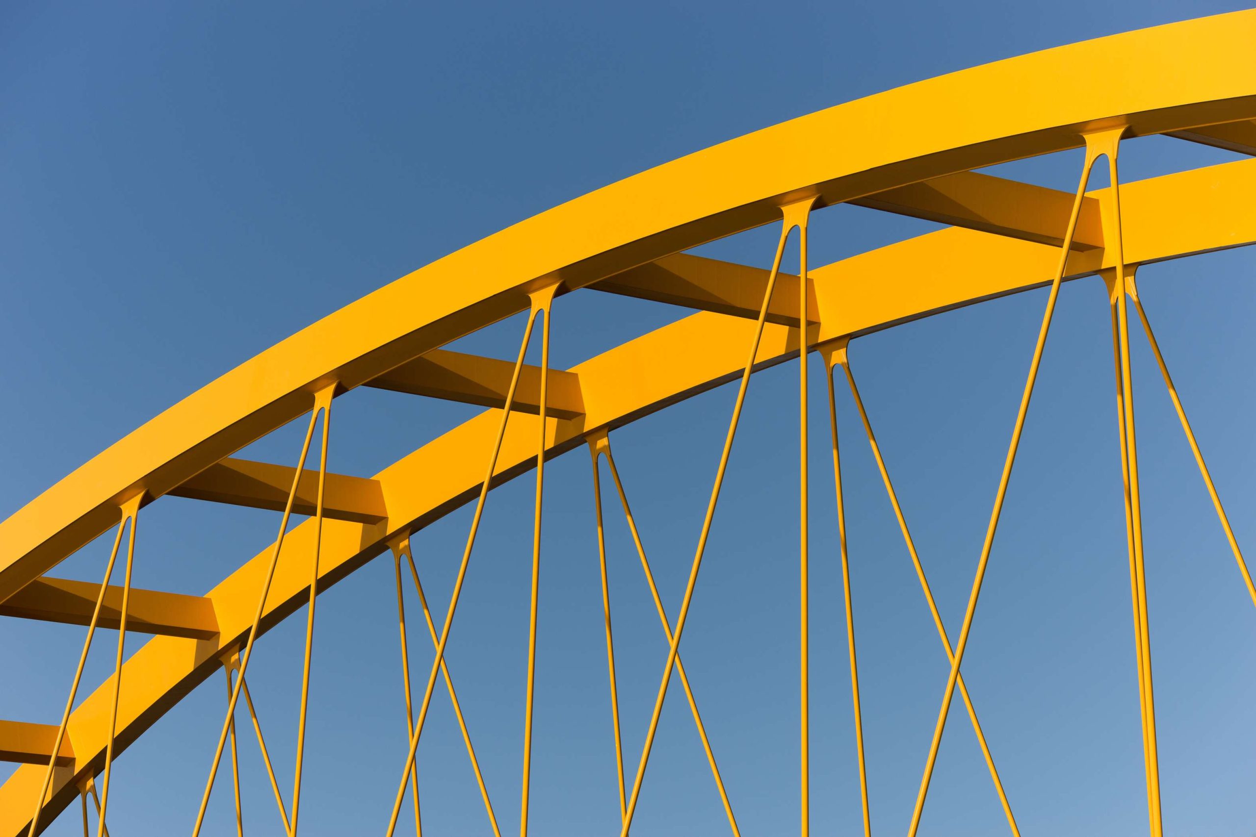 Yellow bridge against a steel blue sky showing beams, girders, columns and cables.