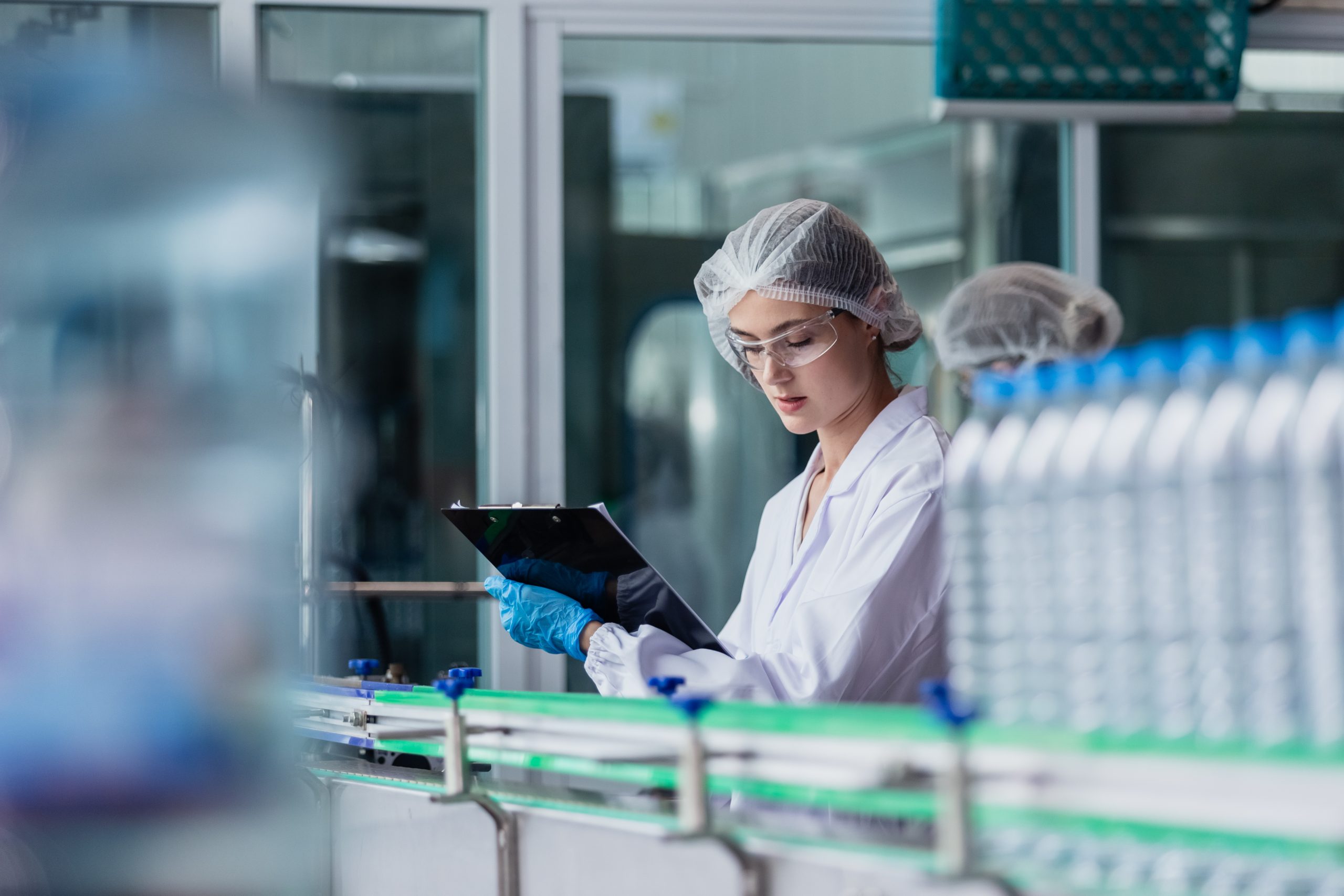 woman factory worker sterile uniform manufacture drink water. Female specialist factory line for processing and checking bottles water. Industrial product manufacturing aqua drink.